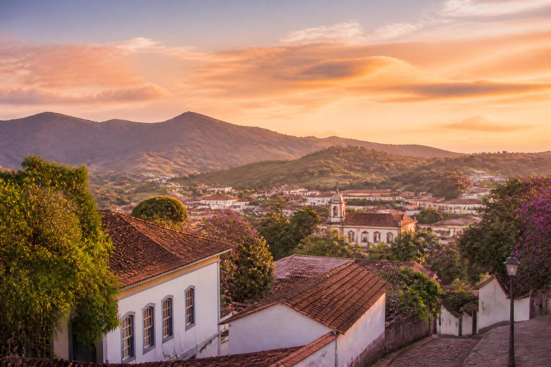 Vista de Santa Rita do Sapucaí ao pôr do sol, com montanhas e telhados coloniais em tons quentes